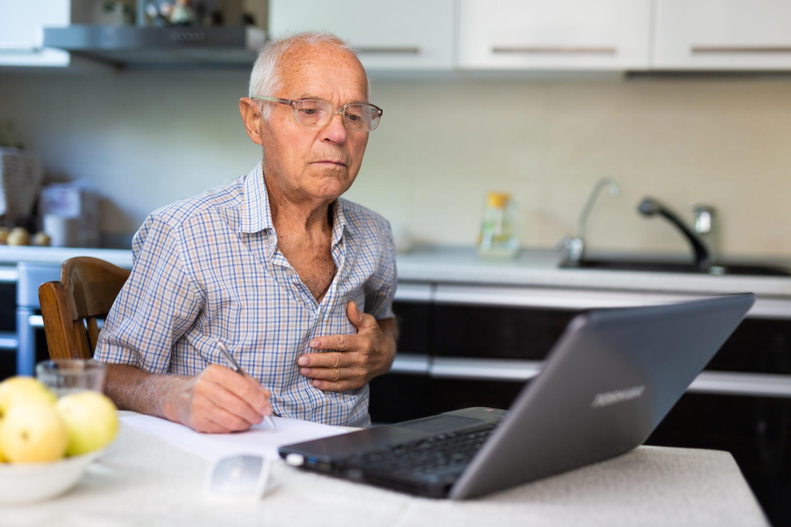 a man sitting at a table with a laptop and writing on paper